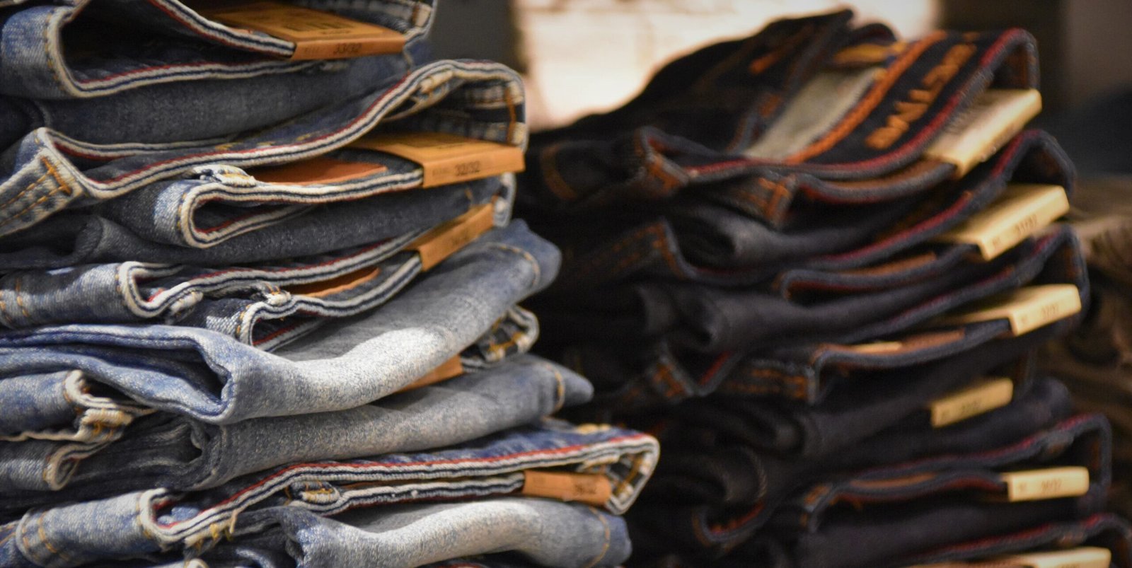 Stacks of folded indigo and blue denim jeans with visible selvedge edges.
